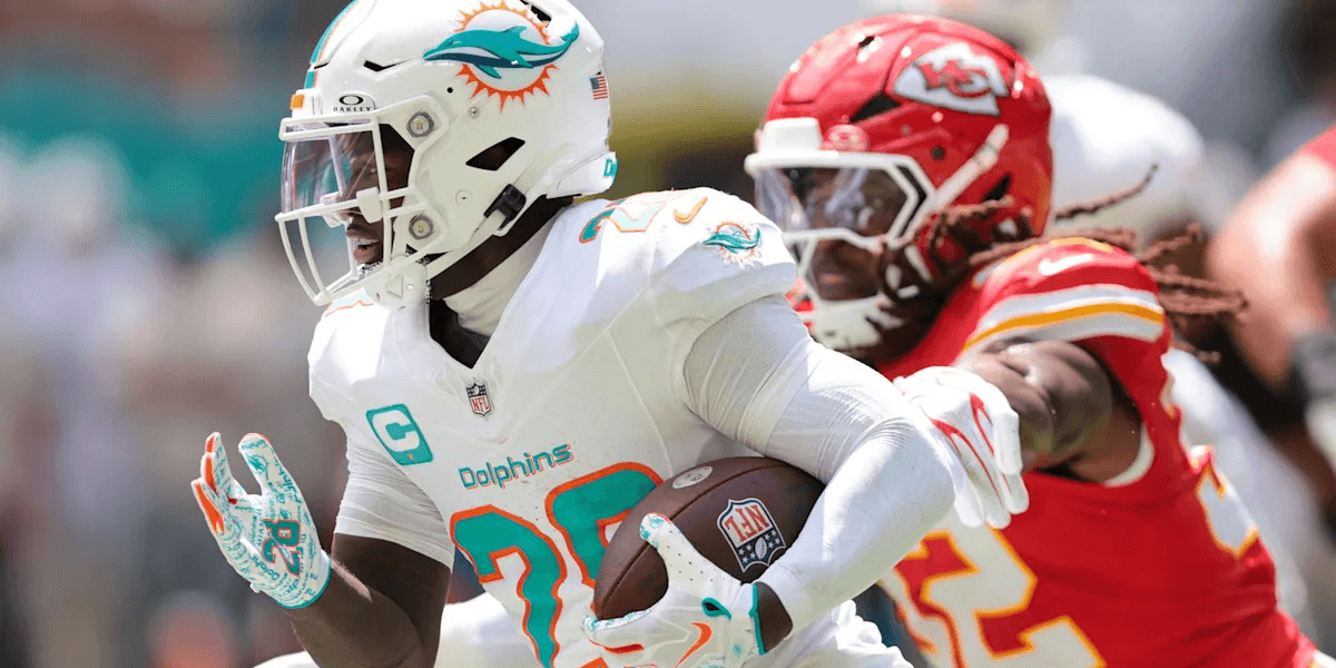 A player in a Dolphins uniform runs with the ball, pursued by a Chiefs defender