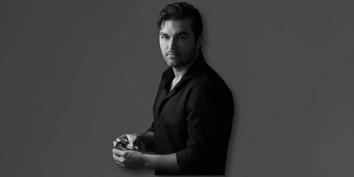 Black-and-white portrait of luxury watch entrepreneur holding a timepiece against a dark studio background.