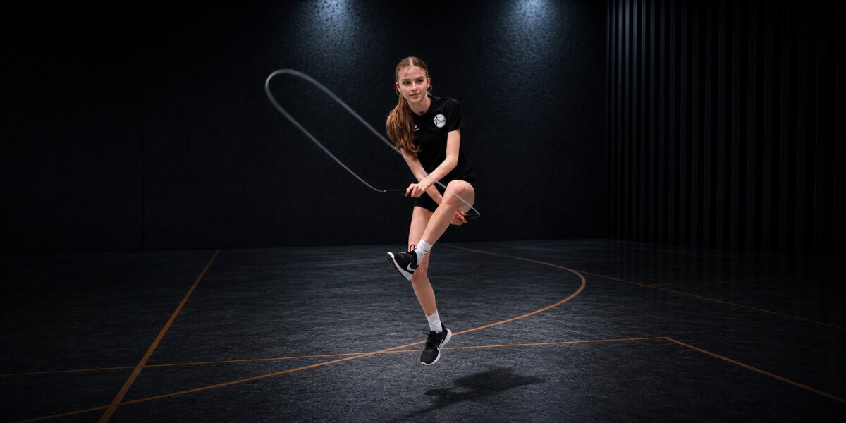 Young athlete jumps rope midair in a dark indoor gym during competitive training.