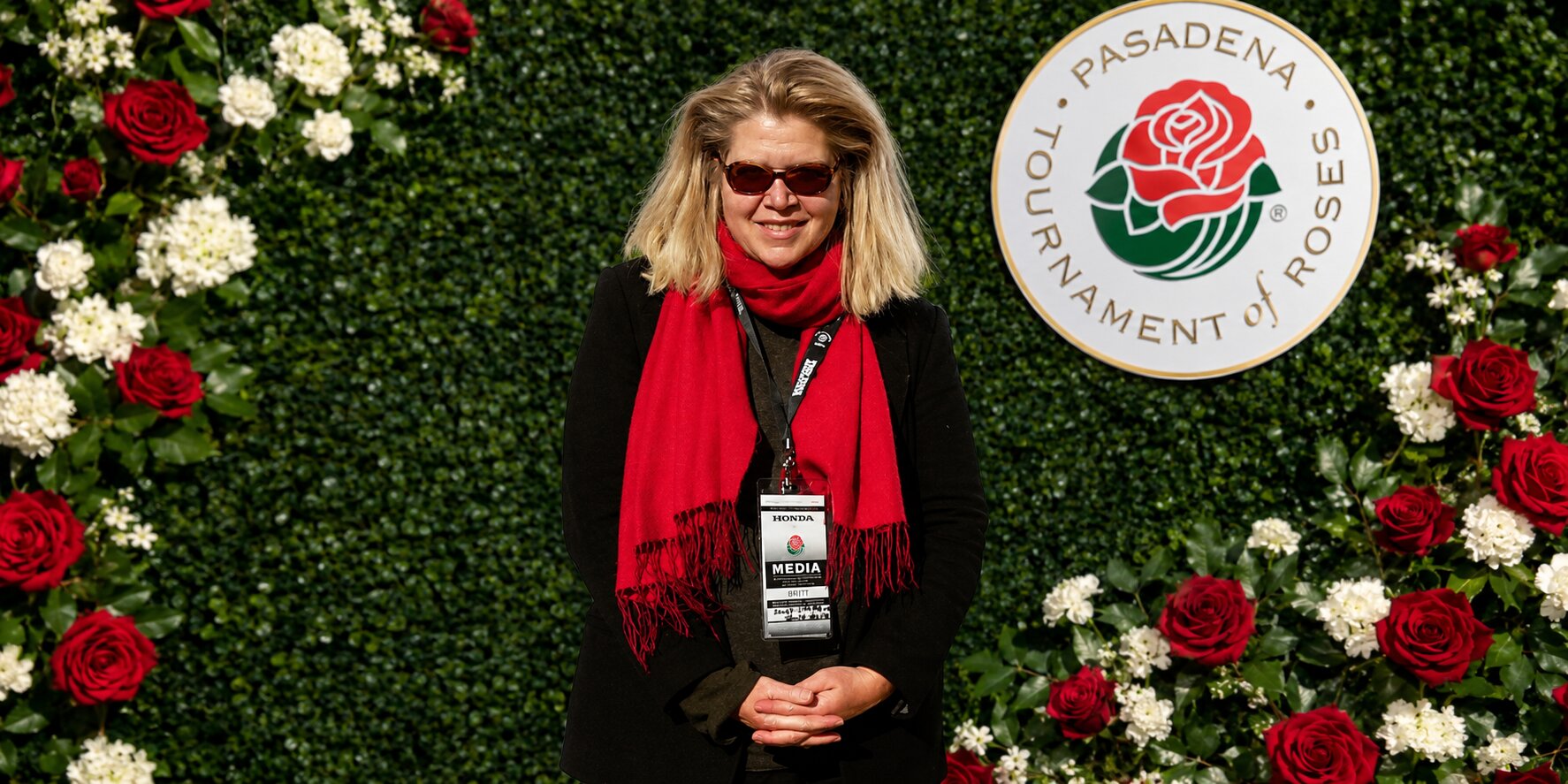 Janet Walker wearing a red scarf and media badge at the Pasadena Tournament of Roses backdrop.