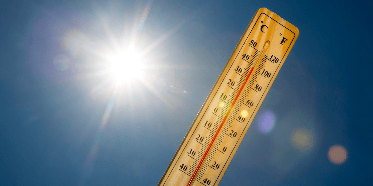 Wooden thermometer showing high temperatures beneath a bright sun in a clear blue sky.
