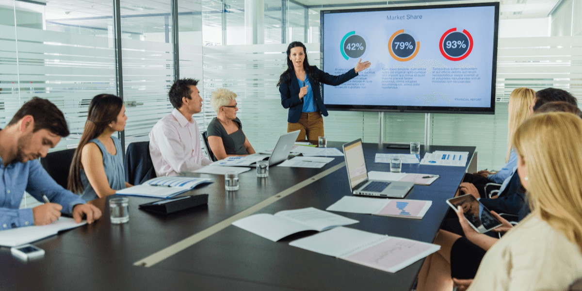 Business team attending a presentation with market share charts displayed on a conference room screen.