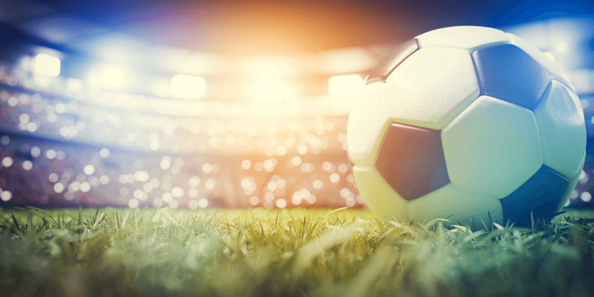 Soccer ball resting on a grass field inside a brightly lit stadium.