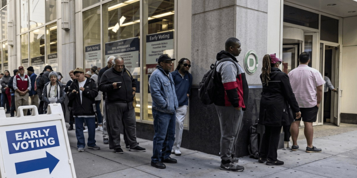 Voters wait in line outside an early voting location with a directional sign in the foreground.