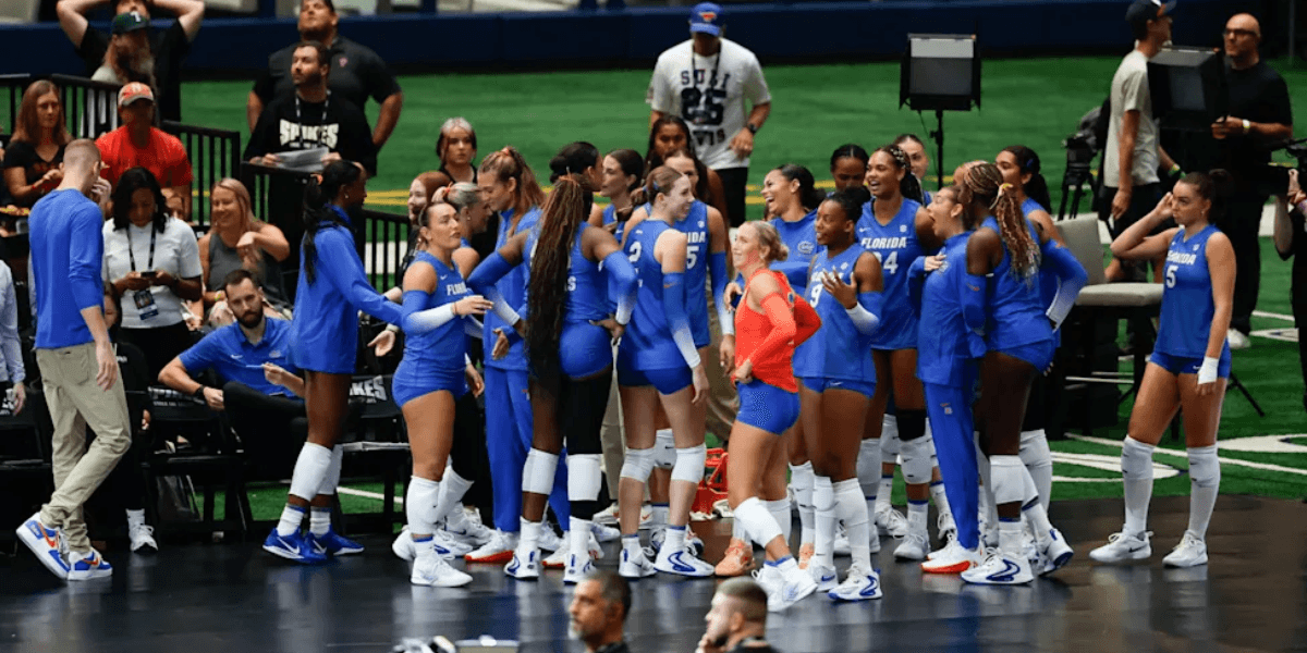 A volleyball team in blue uniforms huddles together, celebrating on the court.