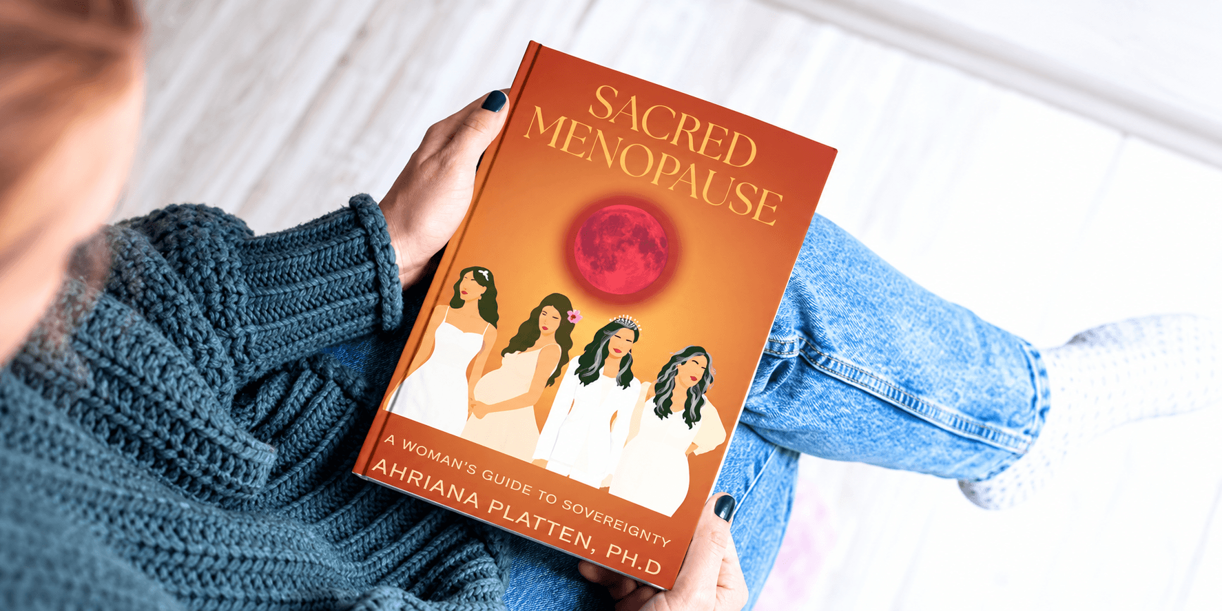Person sitting with a book titled "Sacred Menopause" featuring women and a red moon