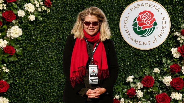 Janet Walker wearing a red scarf and media badge at the Pasadena Tournament of Roses backdrop.