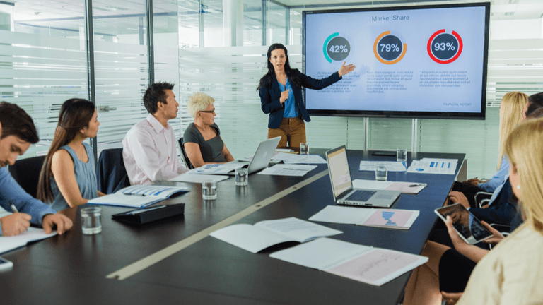 Business team attending a presentation with market share charts displayed on a conference room screen.