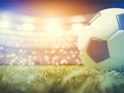 Soccer ball resting on a grass field inside a brightly lit stadium.