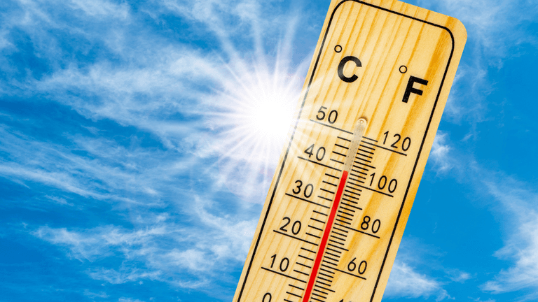 Wooden thermometer displaying temperature against a bright blue sky with sun rays