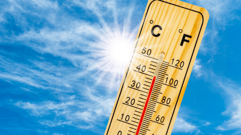 Wooden thermometer displaying temperature against a bright blue sky with sun rays