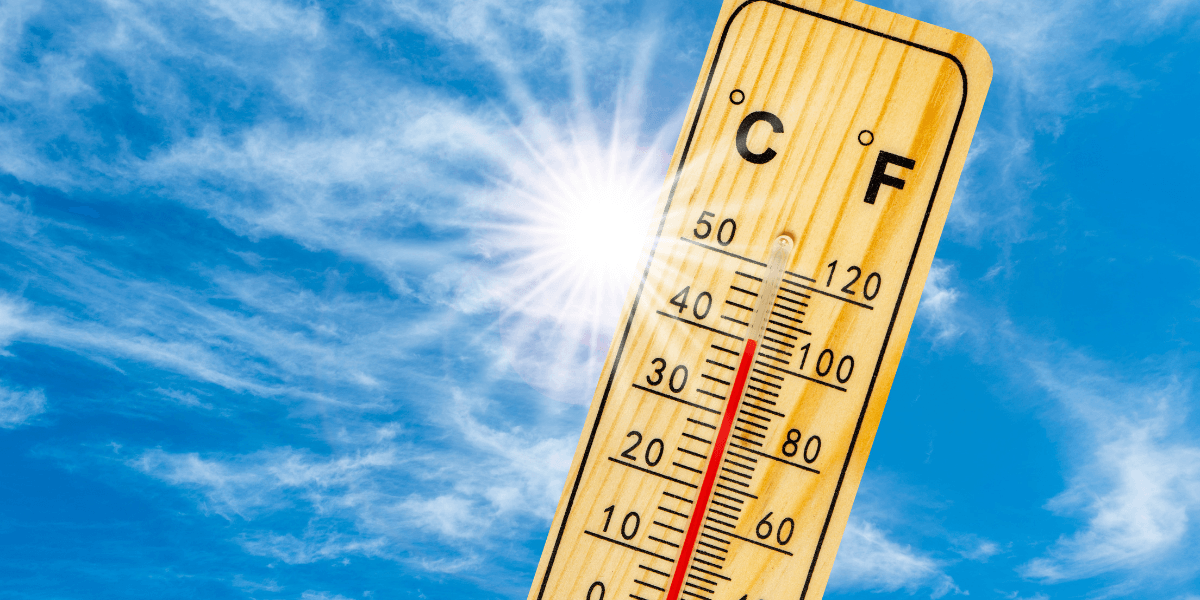 Wooden thermometer displaying temperature against a bright blue sky with sun rays