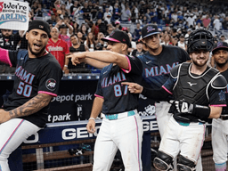 Miami Marlins players celebrate in the dugout, wearing black jerseys with colorful accents