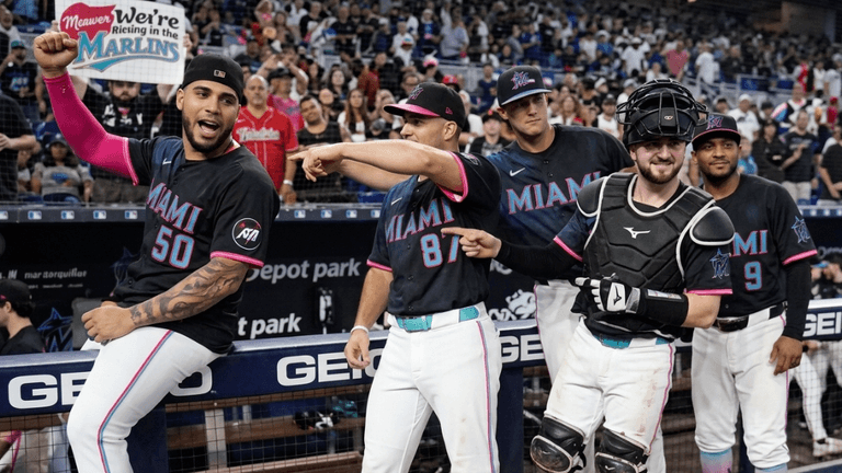 Miami Marlins players celebrate in the dugout, wearing black jerseys with colorful accents