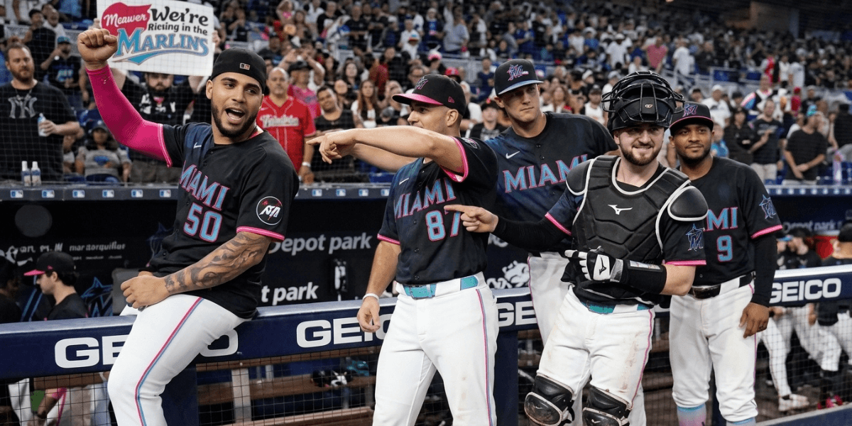 Miami Marlins players celebrate in the dugout, wearing black jerseys with colorful accents