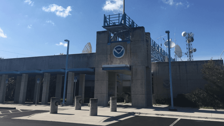 Concrete building with NOAA logo, radar dishes, and a clear blue sky