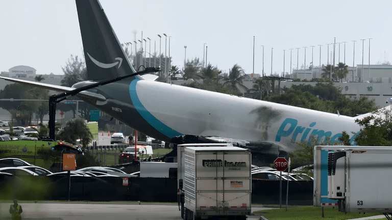 A damaged cargo plane rests on the ground with emergency vehicles nearby