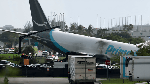 A damaged cargo plane rests on the ground with emergency vehicles nearby