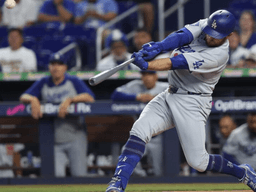 Baseball player in grey uniform swings bat during game with crowd in background