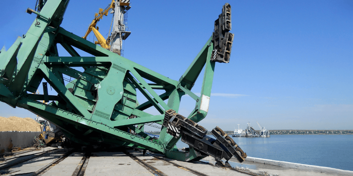 A large green crane lies on its side near a body of water.