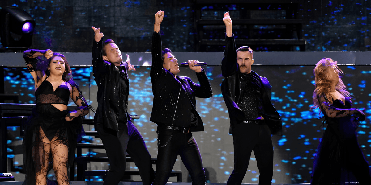 Five performers in matching outfits energetically singing on stage with bright lights