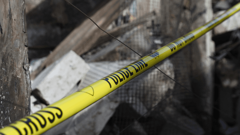 Yellow police tape near a collapsed building with debris scattered around