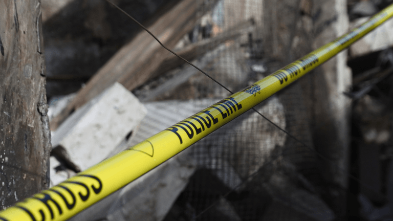 Yellow police tape near a collapsed building with debris scattered around