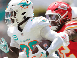 A player in a Dolphins uniform runs with the ball, pursued by a Chiefs defender