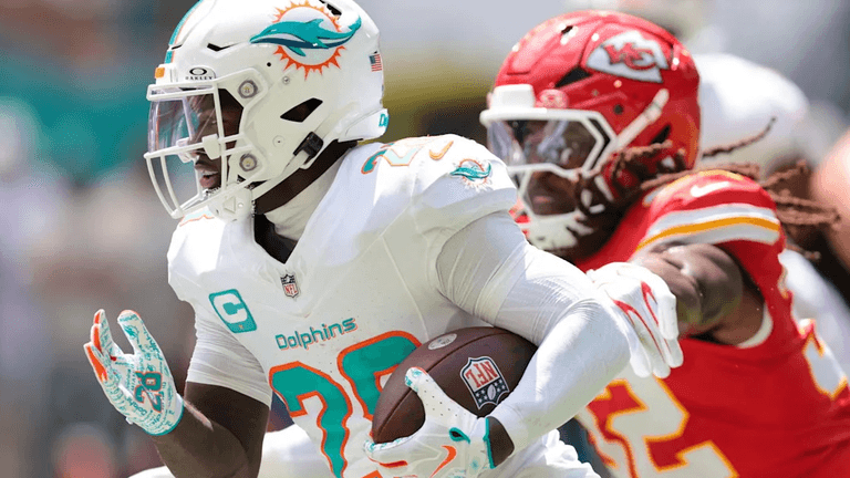 A player in a Dolphins uniform runs with the ball, pursued by a Chiefs defender