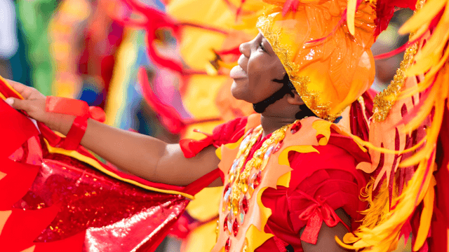 Child in vibrant orange and red costume, joyfully participating in a colorful parade