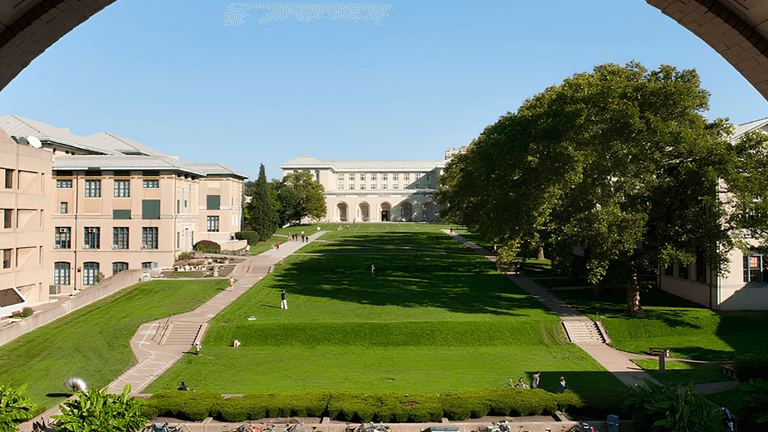 View of a green grassy slope with buildings and trees under a clear blue sky