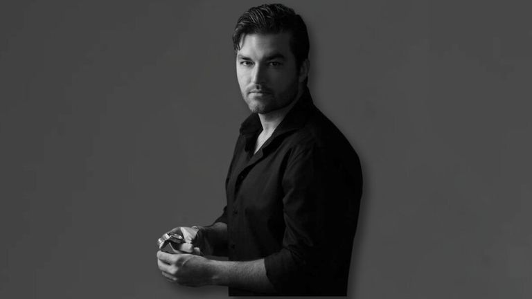Black-and-white portrait of luxury watch entrepreneur holding a timepiece against a dark studio background.