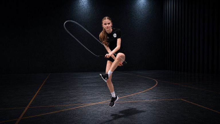 Young athlete jumps rope midair in a dark indoor gym during competitive training.