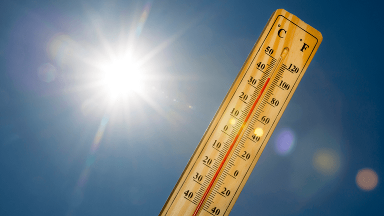 Wooden thermometer showing high temperatures beneath a bright sun in a clear blue sky.