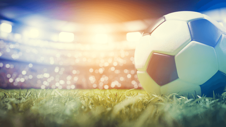 Soccer ball resting on a grass field inside a brightly lit stadium.
