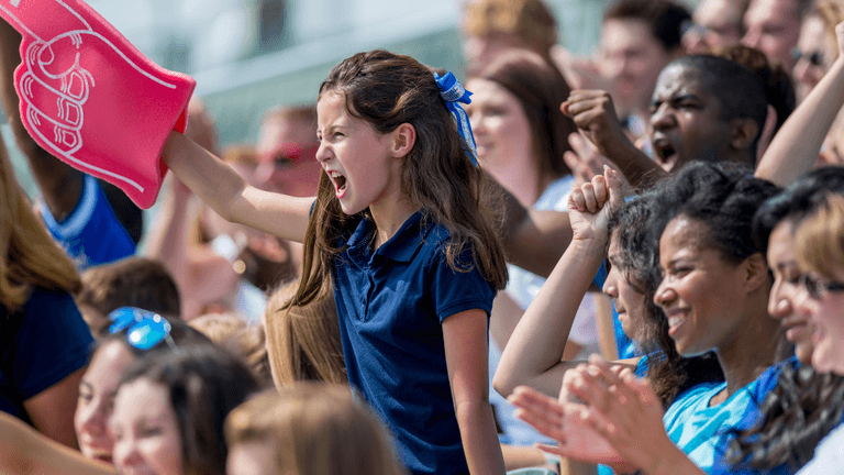Young soccer fan cheering with a foam finger in a crowded stadium during a match.