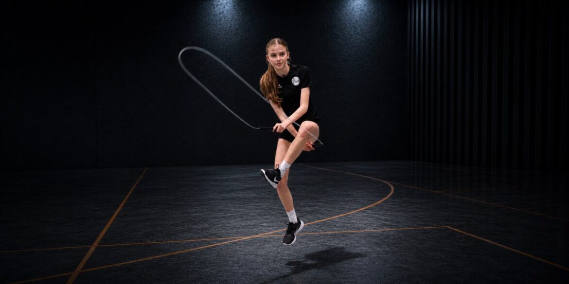 Young athlete jumps rope midair in a dark indoor gym during competitive training.