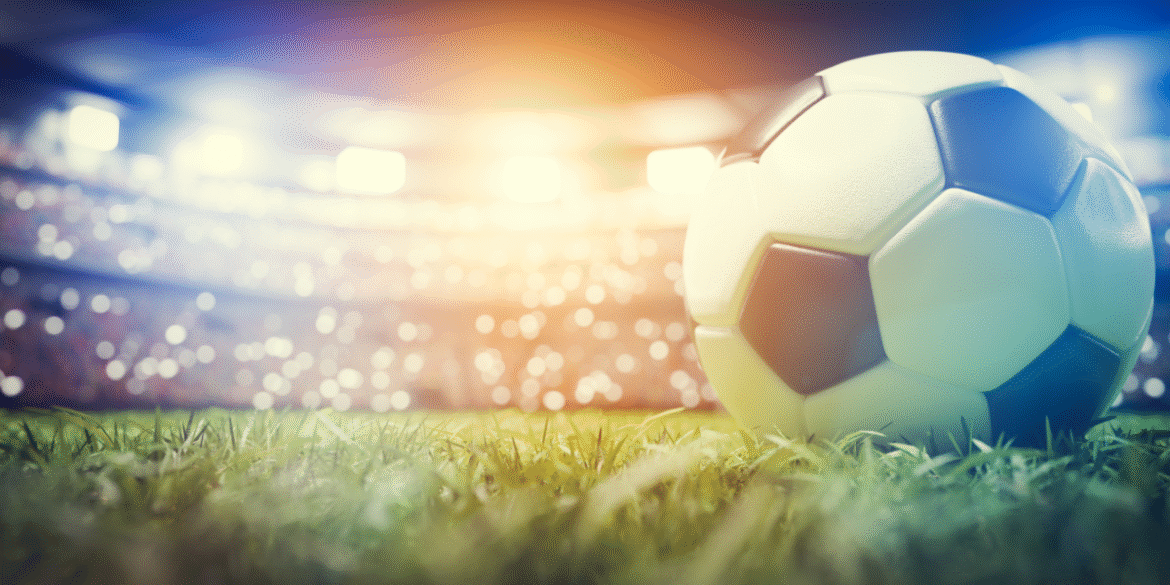 Soccer ball resting on a grass field inside a brightly lit stadium.