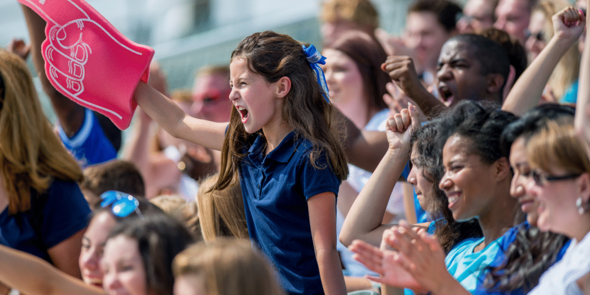 Young soccer fan cheering with a foam finger in a crowded stadium during a match.