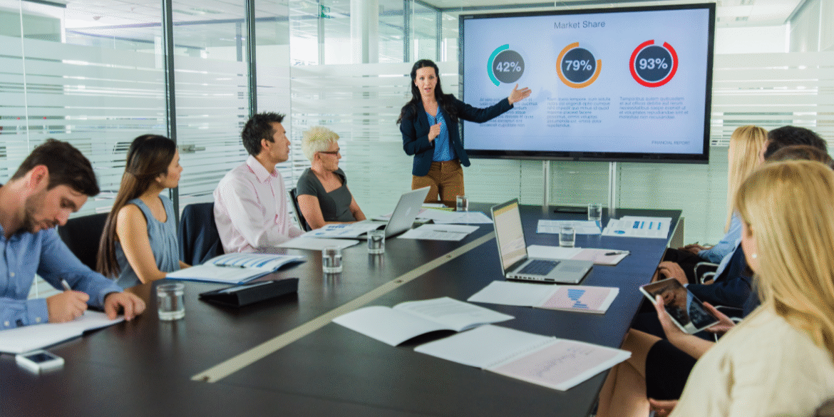 Business team attending a presentation with market share charts displayed on a conference room screen.