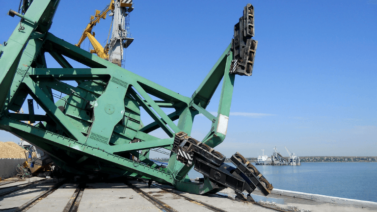 A large green crane lies on its side near a body of water.