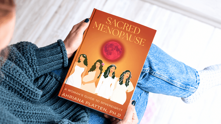Person sitting with a book titled "Sacred Menopause" featuring women and a red moon