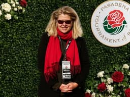 Janet Walker wearing a red scarf and media badge at the Pasadena Tournament of Roses backdrop.